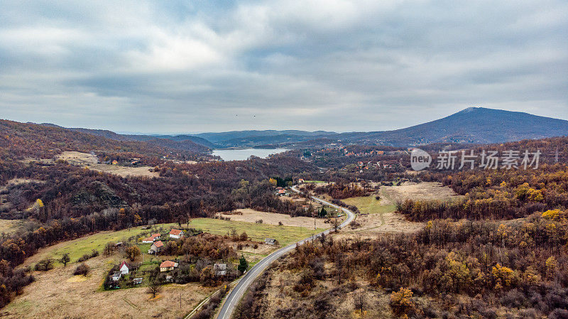 Borsko jezero - Flying over the empty autumn road with the bright trees in the green, orange and red tones - Top view of the bright autumn colors of the forest in eastern Serbia - 4K drone shot